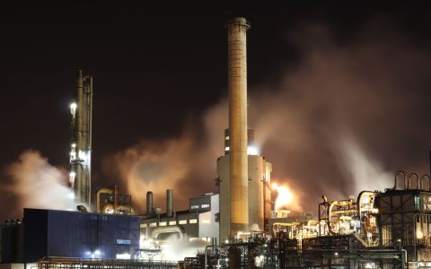 A nighttime view of an industrial factory with smokestacks emitting smoke, highlighting energy production and pollution.