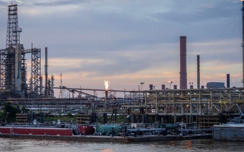 A large industrial refinery complex next to a river with a sunset backdrop.