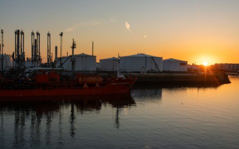 A picturesque view of an industrial port and tanker ship at sunrise, creating a stunning silhouette.