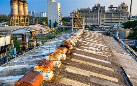 Exterior of aged shabby factory with rusty industrial buildings and mechanisms with pipes in town