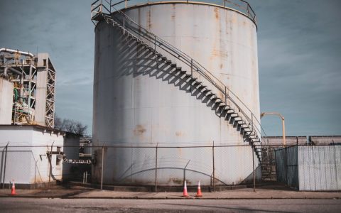 Industrial storage tank with metal stairs in an outdoor facility under clear sky.