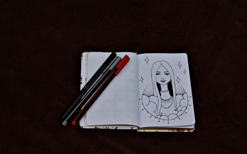 Open sketchbook with a detailed artwork and pens on a dark background, perfect for creative inspiration.