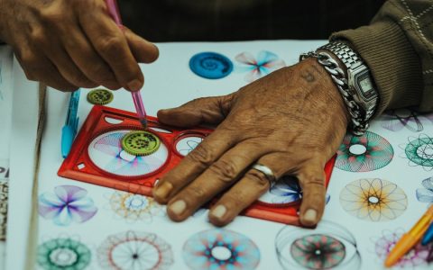 Close-up of hands creating vibrant spirograph patterns with pencils, showcasing creativity and precision.