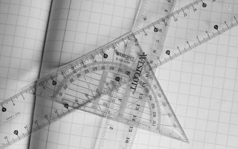 Monochrome photo of rulers and protractor on graph paper, emphasizing geometry.