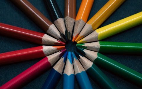 A vivid display of multicolored pencils arranged in a circular pattern on a dark background.