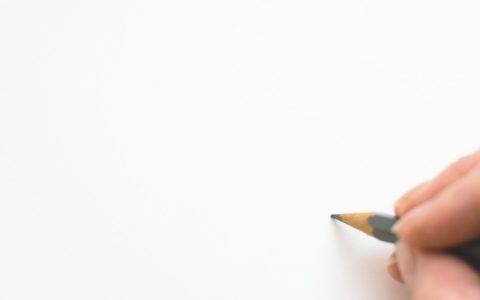Close-up of a hand sketching on white paper with a pencil, emphasizing creativity.