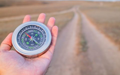 Hand holding a compass guiding along a dusty path outdoors. Perfect for travel and exploration themes.