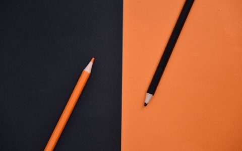 An artistic flat lay of orange and black pencils on orange and black background.