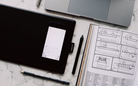 A modern workspace featuring a drawing tablet, smartphone, laptop, and design documents on a marble desk.