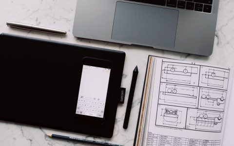 Cellphone put on black tablet located near sketchbook showing drawn plan and portable computer on marble table put in organized order