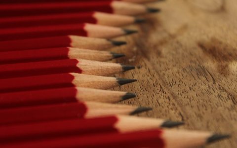 Neatly sharpened red pencils perfectly aligned on a wooden surface, showcasing symmetry and precision.