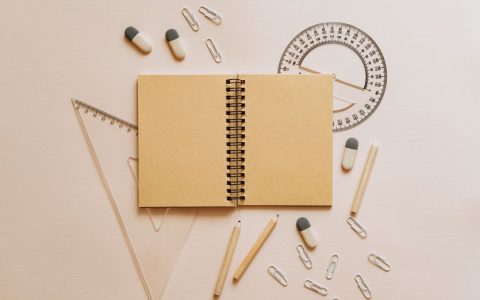Flat lay of school stationery including a notebook, pencils, and geometry tools on a beige background.