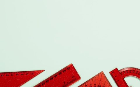 Red plastic rulers and protractors arranged on a soft pastel green background, ideal for school or office themes.