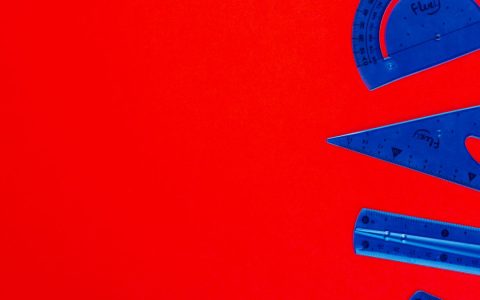 Blue plastic protractor, ruler, and set square on a vivid red background, perfect for educational themes.