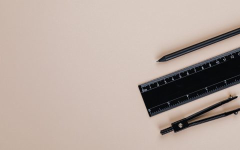 Minimalist flat lay of a compass, pencil, and ruler on a cream-colored background.