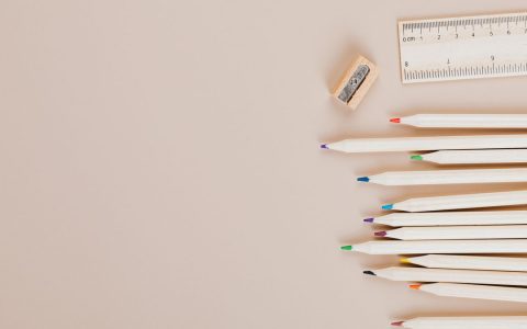 Flat lay composition of colored pencils, ruler, and sharpener on a beige background.