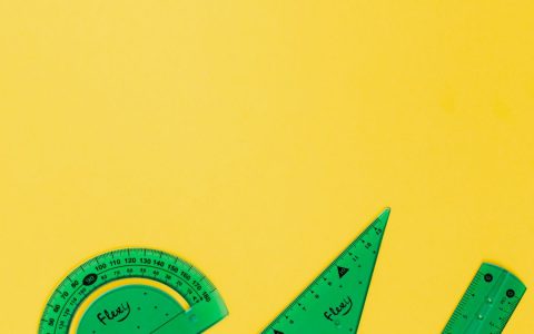 Green protractor, set square, and ruler on a yellow surface, perfect for educational themes.