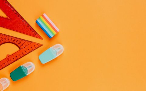 Vibrant flat lay of stationery items, including rulers and erasers, on an orange background.