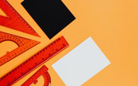 Vibrant orange rulers and geometric tools on an orange background with black and white cards.