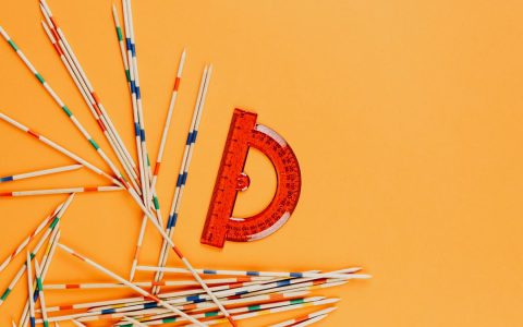 A vibrant arrangement of a red protractor and colorful striped sticks scattered on an orange background.