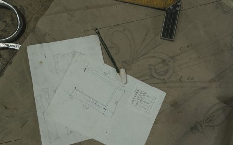 Detailed view of architectural sketches and drawing tools on a workbench, reflecting a crafting workspace.