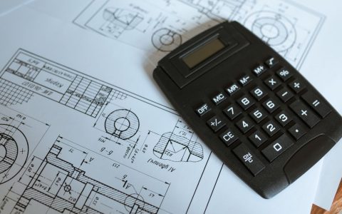 Close-up of a calculator resting on technical engineering blueprints, showcasing precise calculations.