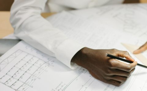 Architect working on detailed floor plans with a pencil and set square, captured in bright indoor setting.
