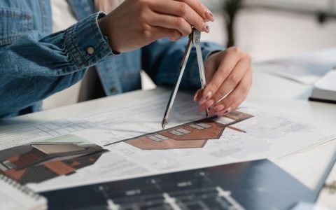 A creative professional using a compass on blueprints at an office desk.