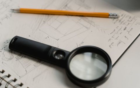 A magnifying glass and pencil on a hand-drawn architectural sketch pad, suggesting scrutiny and planning.