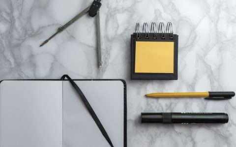 Flat lay of school supplies including compass, notebook, pen, and sticky notes on a marble surface.