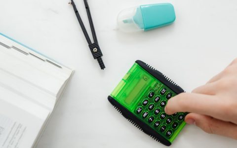 Close-up of a hand using a green calculator with stationery for studies or business calculations.