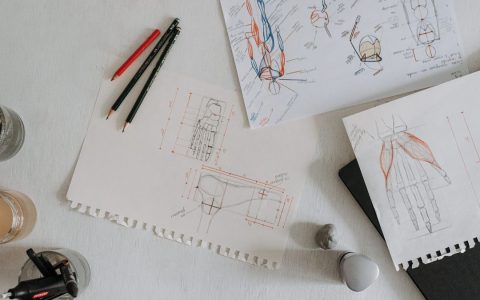 Top view of anatomical sketches with drawing tools on a desk, showcasing artistic process.
