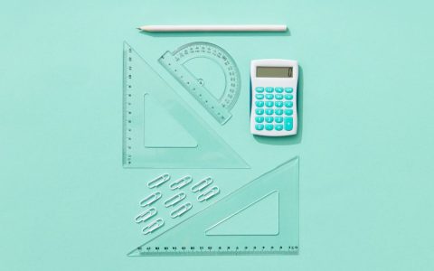 Flat lay of school supplies including calculator, rulers, and pencil on pastel background.