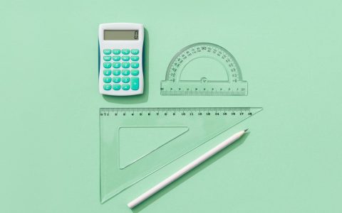 A minimalist flat lay of school supplies on a green background including a calculator, rulers, and pencil.