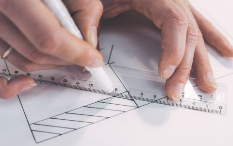 Close-up of hands drawing precise lines with ruler and pen, emphasizing accuracy.