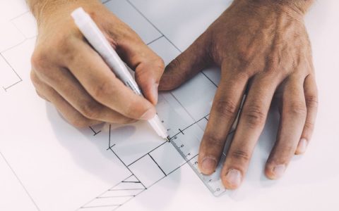 Hands sketching architectural plans with precision using ruler and pen on paper.