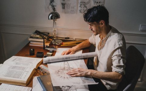 Young architect at a desk working on blueprint designs under lamp light.