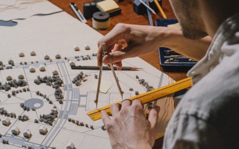 Architect meticulously working on a detailed scale model with compass and ruler.