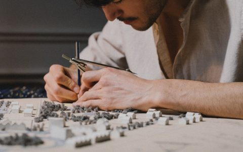 Architect focused on creating a detailed model using a compass indoors, showcasing precision and creativity.