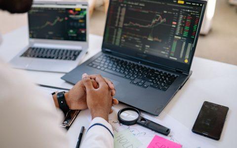 Business professional analyzing stock market data on dual laptops in an office.