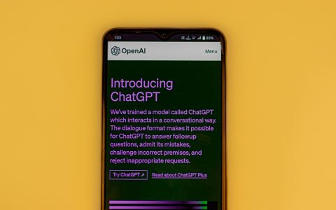 Mobile phone displaying the ChatGPT introduction screen with OpenAI branding on a yellow background.