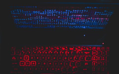 Dark-themed laptop setup with a red glowing keyboard and code on screen, ideal for tech enthusiasts.