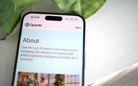 Close-up shot of a smartphone screen showing the OpenAI website with greenery in the background.
