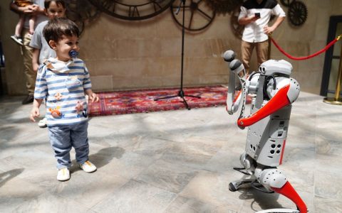A young boy engages with a humanoid robot during an indoor tech exhibition, symbolizing future innovation.