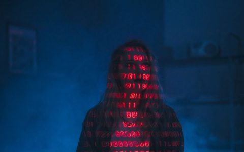 A mysterious silhouette with red binary code projected over the face, set against a dark, moody background.