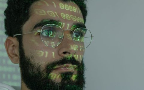 A bearded man with digital binary code projected on his face, symbolizing cybersecurity and technology.