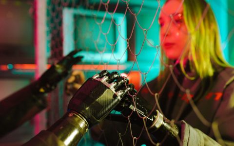 A woman interacts with robotic hands through a mesh displaying a neon cyberpunk atmosphere.