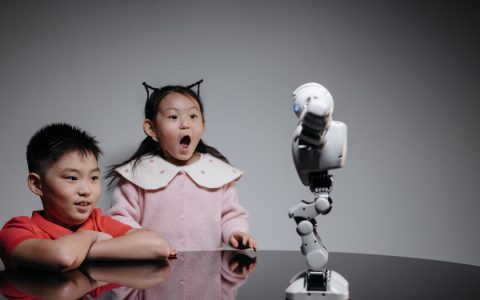 Two children fascinated by a toy robot, showcasing excitement and curiosity indoors.