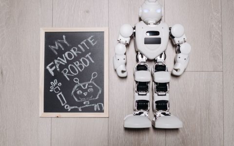 Overhead shot of a robot toy alongside a chalkboard drawing, on a light wooden floor.