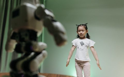 An Asian child interacts with a humanoid robot indoors, embracing innovation and play.